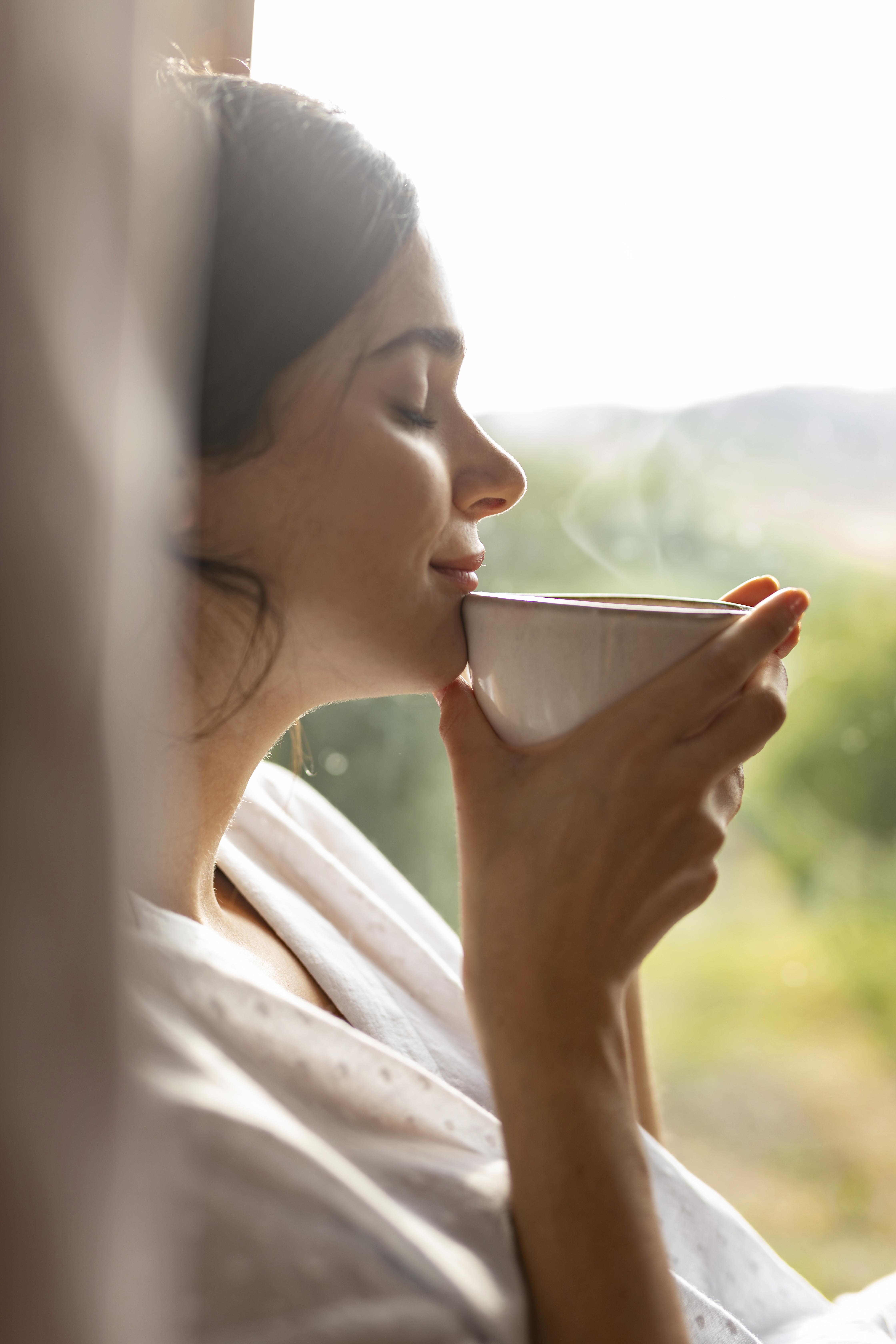 Young woman drinking coffee, window behind with green area